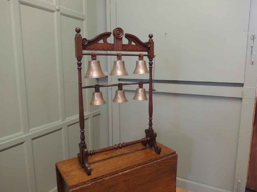 A Victorian carved walnut rack displaying six tuned brass bells arranged across two horizontal tiers on turned wooden uprights. View IV