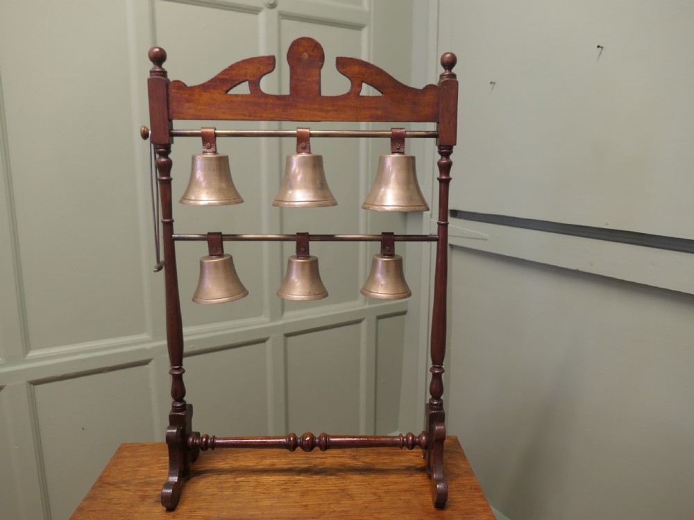 A Victorian carved walnut rack displaying six tuned brass bells arranged across two horizontal tiers on turned wooden uprights. View V