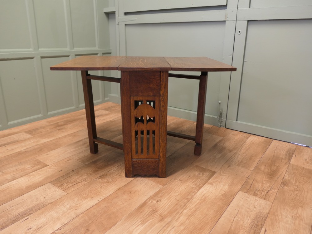 An Arts and Crafts golden oak drop-leaf dining table with pierced cutout side panels. View II