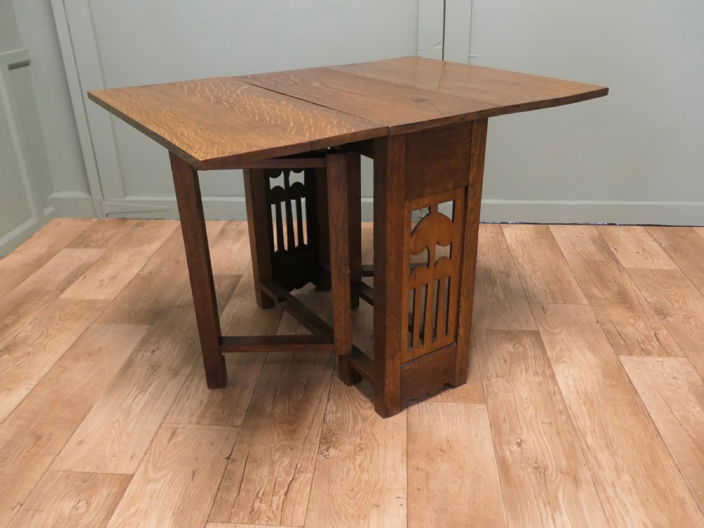 An Arts and Crafts golden oak drop-leaf dining table with pierced cutout side panels. View III
