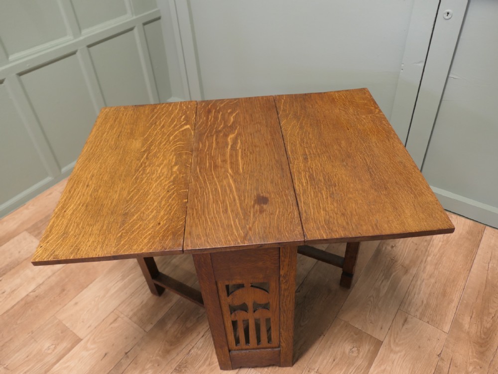 An Arts and Crafts golden oak drop-leaf dining table with pierced cutout side panels. View V