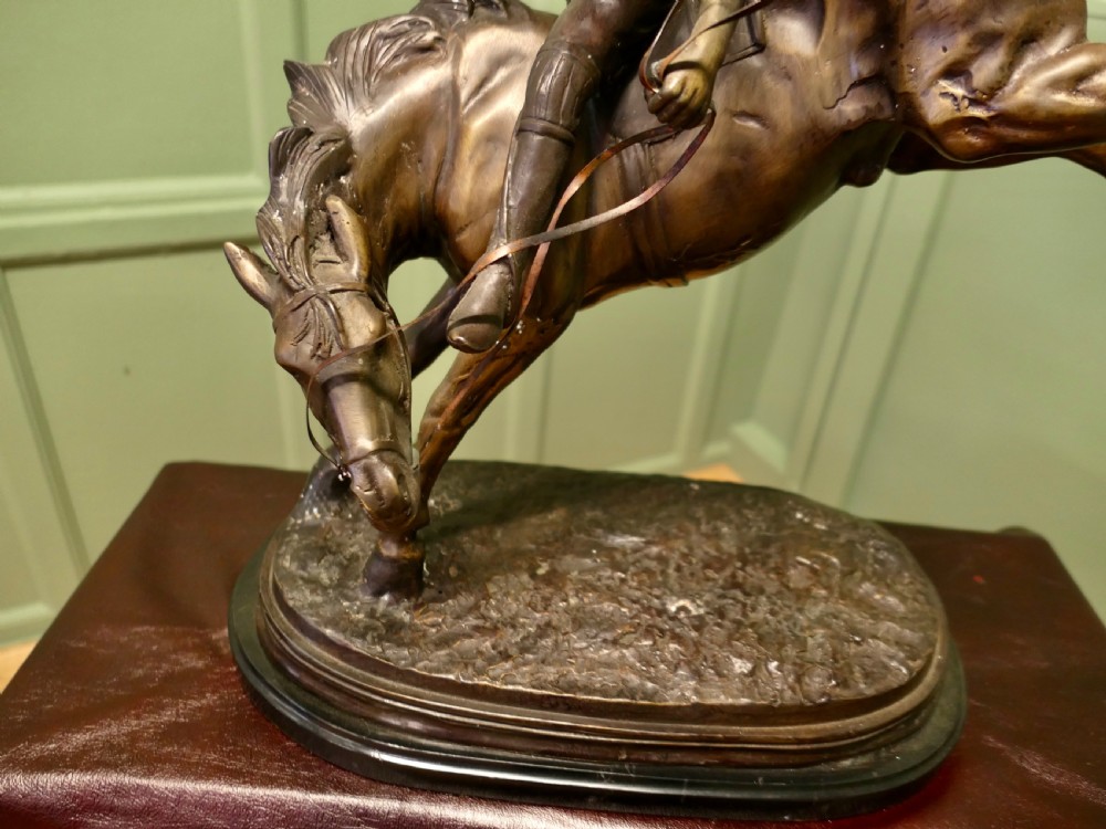 A dark bronze sculpture depicting a polo player wearing a helmet, riding a bucking pony mounted on an oval base. View II