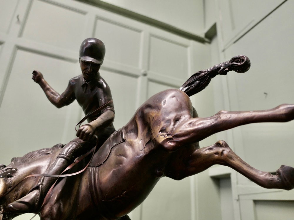 A dark bronze sculpture depicting a polo player wearing a helmet, riding a bucking pony mounted on an oval base. View III