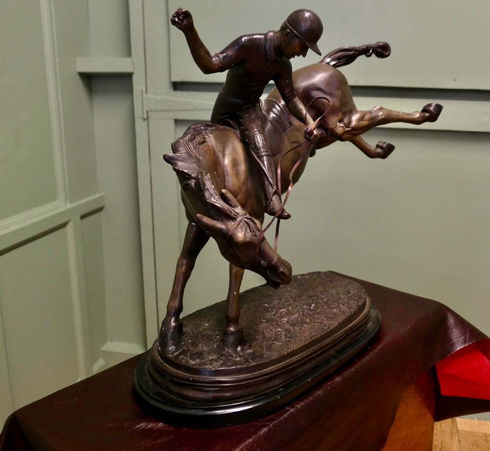 A dark bronze sculpture depicting a polo player wearing a helmet, riding a bucking pony mounted on an oval base. View IV