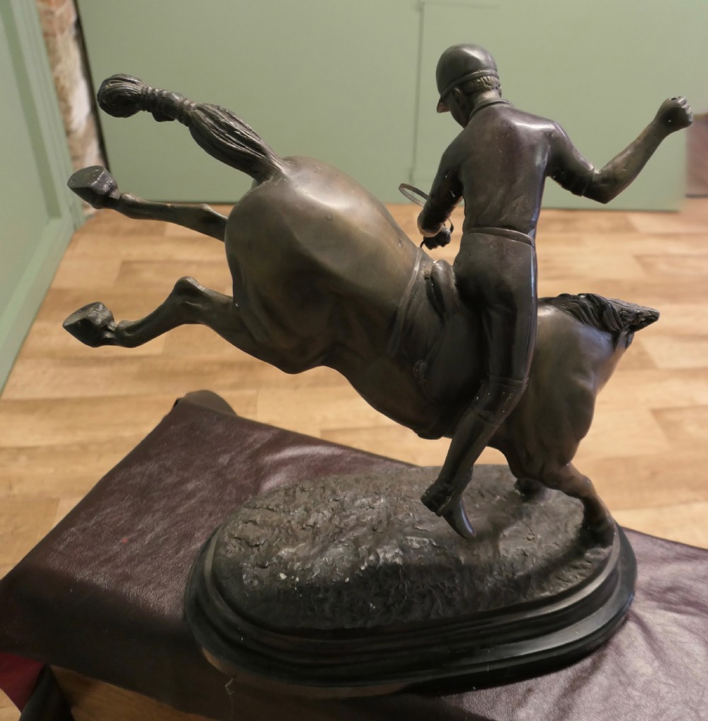 A dark bronze sculpture depicting a polo player wearing a helmet, riding a bucking pony mounted on an oval base. View V