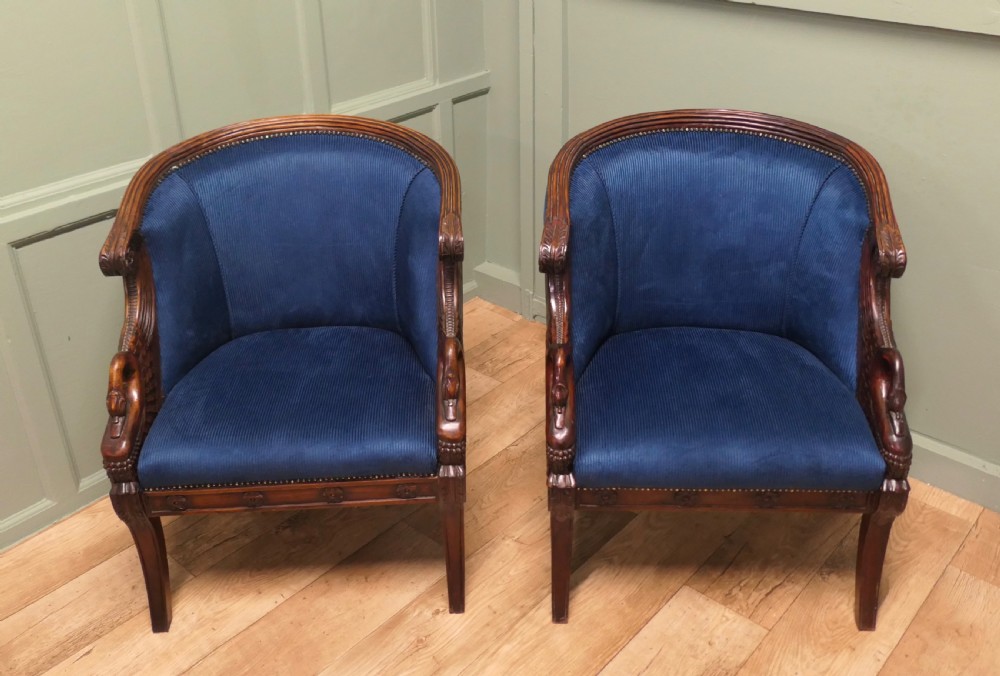 A pair of Victorian tub chairs with blue upholstery and carved mahogany frames featuring carved swan neck armrests.