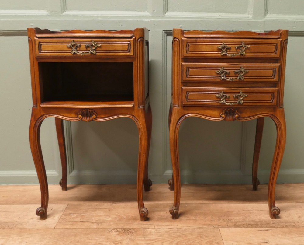 A pair of French cherry wood bedside tables featuring cabriole legs, brass handles, and carved shell motifs, one configured with an open shelf and the other with three drawers.