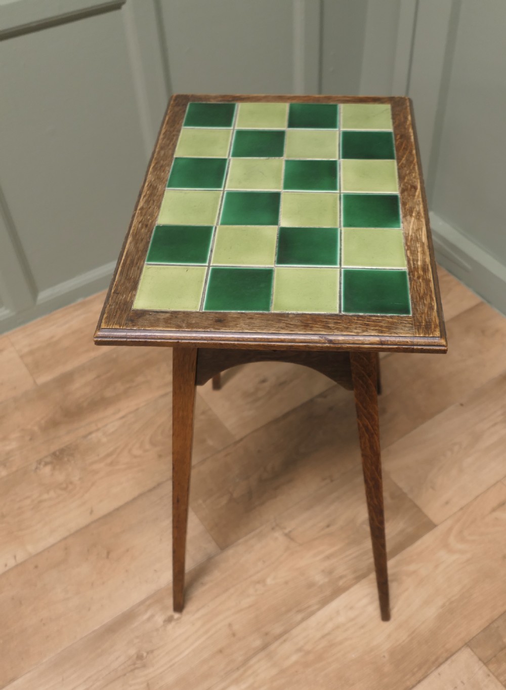 An Arts and Crafts oak occasional table featuring a green checkerboard ceramic tiled top, tapered legs, and heart-shaped cutouts on the apron. View IV
