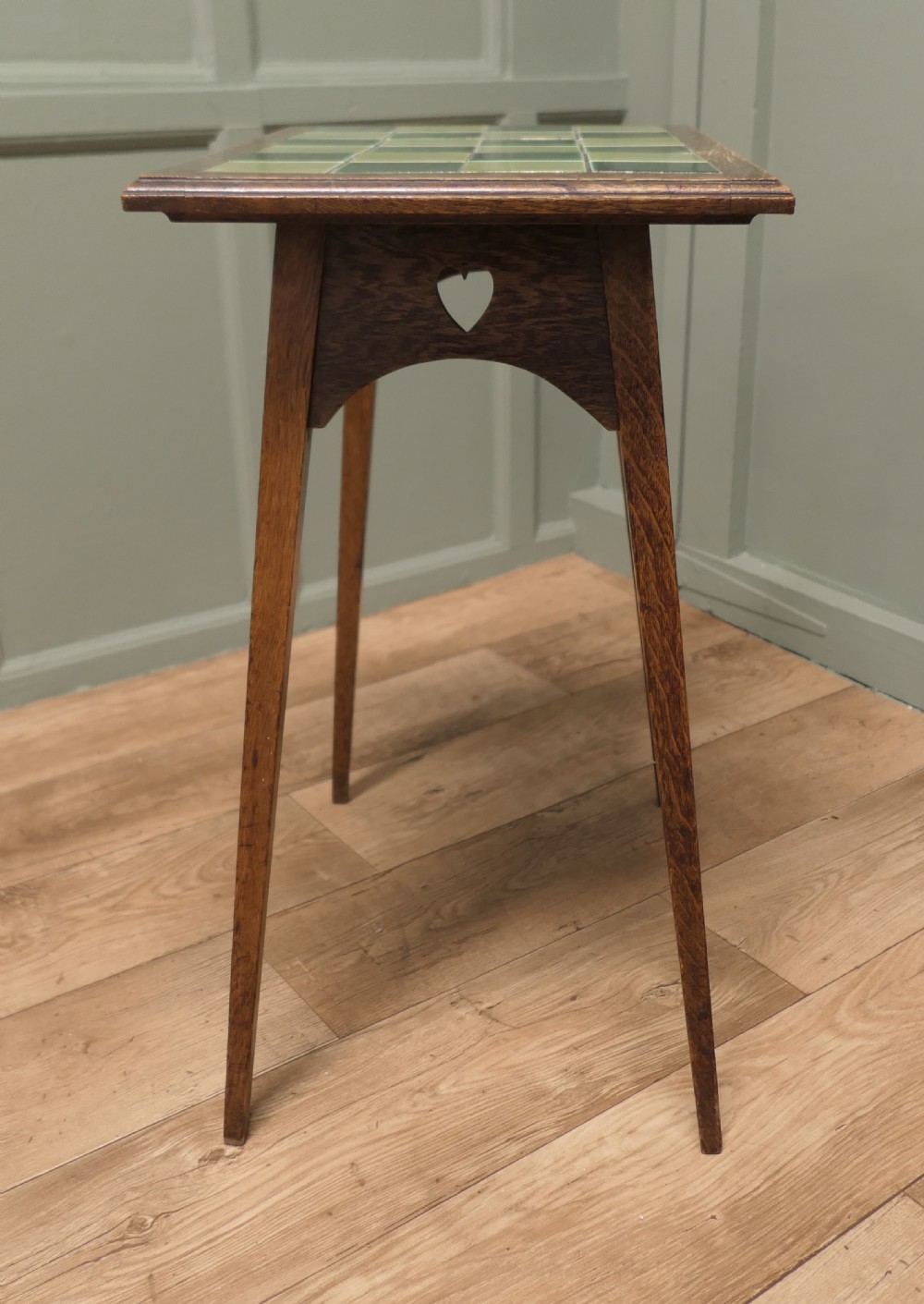 An Arts and Crafts oak occasional table featuring a green checkerboard ceramic tiled top, tapered legs, and heart-shaped cutouts on the apron. View V