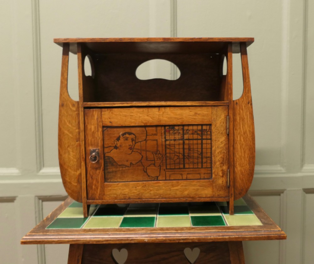 An Arts and Crafts oak wall cabinet featuring a single door decorated with a pyrography panel of a seated figure, framed by shaped side supports and a top shelf.