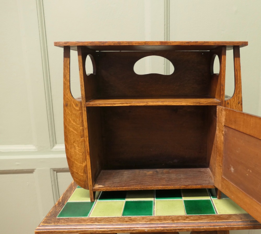 An Arts and Crafts oak wall cabinet featuring a single door decorated with a pyrography panel of a seated figure, framed by shaped side supports and a top shelf. View IV