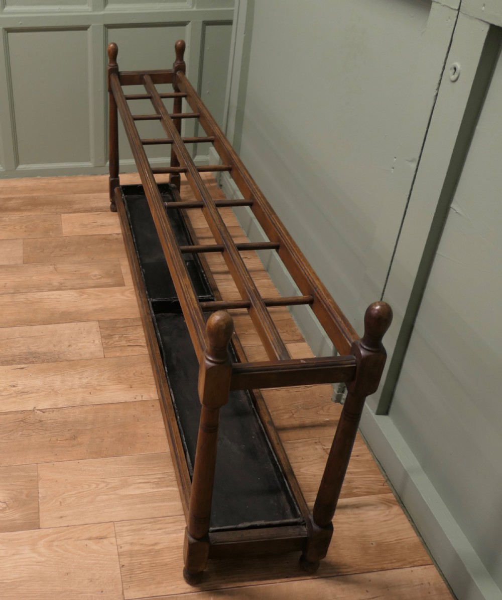 A six-foot long Arts and Crafts wooden umbrella stand with slatted compartment dividers, turned finials, and a removable metal drip tray base. View II