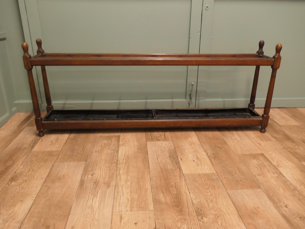 A six-foot long Arts and Crafts wooden umbrella stand with slatted compartment dividers, turned finials, and a removable metal drip tray base. View IV