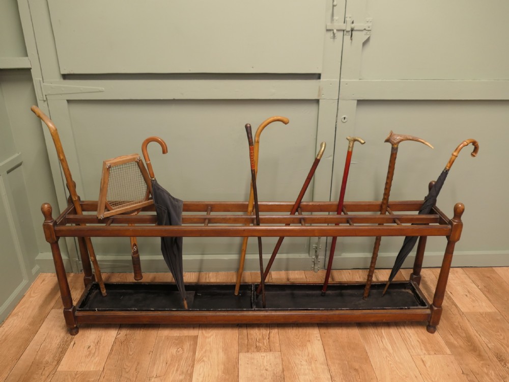 A six-foot long Arts and Crafts wooden umbrella stand with slatted compartment dividers, turned finials, and a removable metal drip tray base. View V