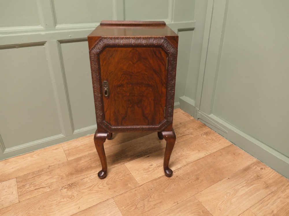 An Art Deco burr walnut bedside cabinet featuring a carved door frame, brass latch, low gallery back, and four cabriole legs. View III