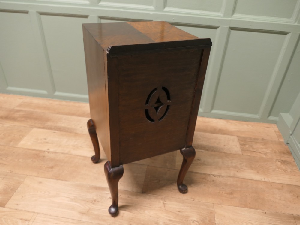 An Art Deco burr walnut bedside cabinet featuring a carved door frame, brass latch, low gallery back, and four cabriole legs. View IV