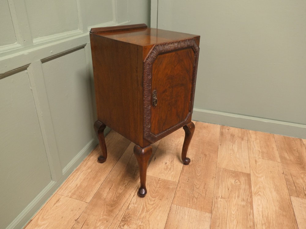 An Art Deco burr walnut bedside cabinet featuring a carved door frame, brass latch, low gallery back, and four cabriole legs. View V