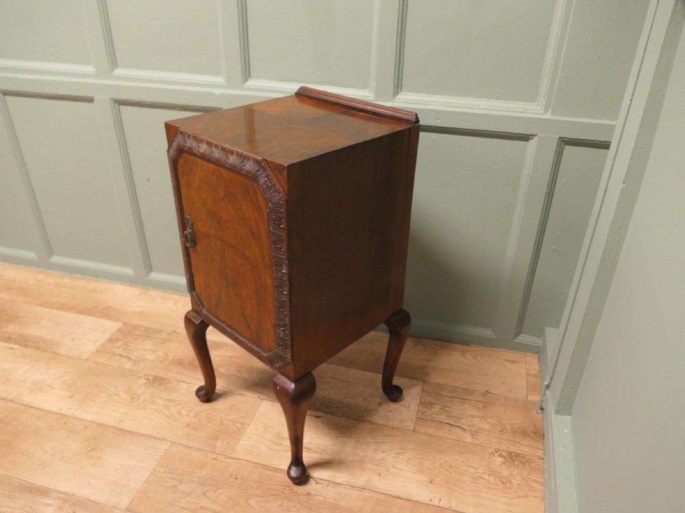 An Art Deco burr walnut bedside cabinet featuring a carved door frame, brass latch, low gallery back, and four cabriole legs. View VI