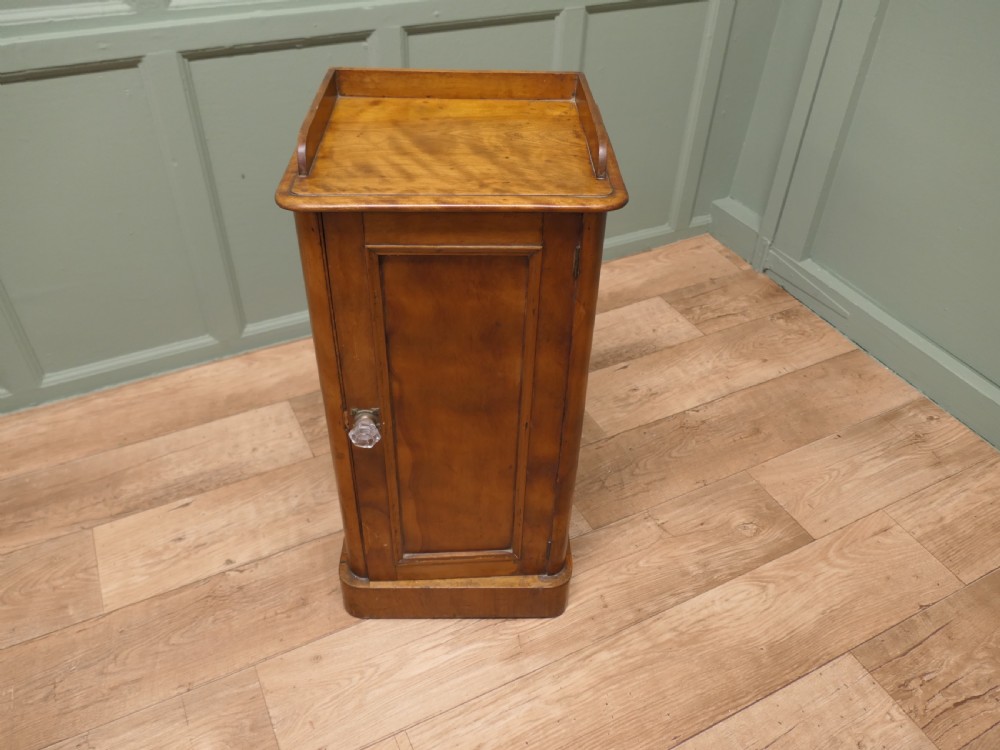 A Victorian birch bedside cupboard featuring a three-sided gallery top, a single panelled door with a glass handle, and a solid plinth base.