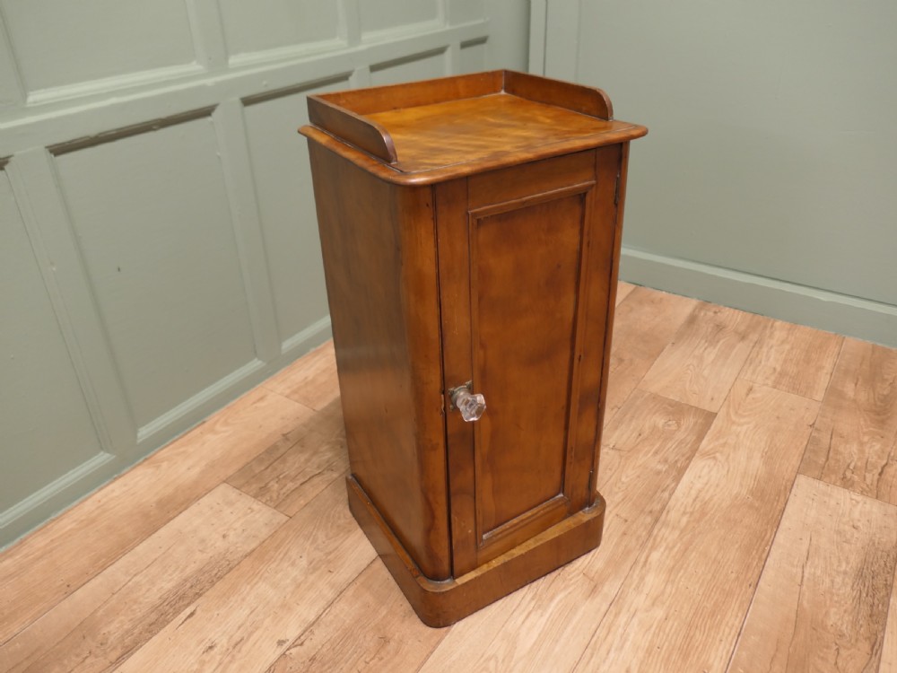 A Victorian birch bedside cupboard featuring a three-sided gallery top, a single panelled door with a glass handle, and a solid plinth base. View IV