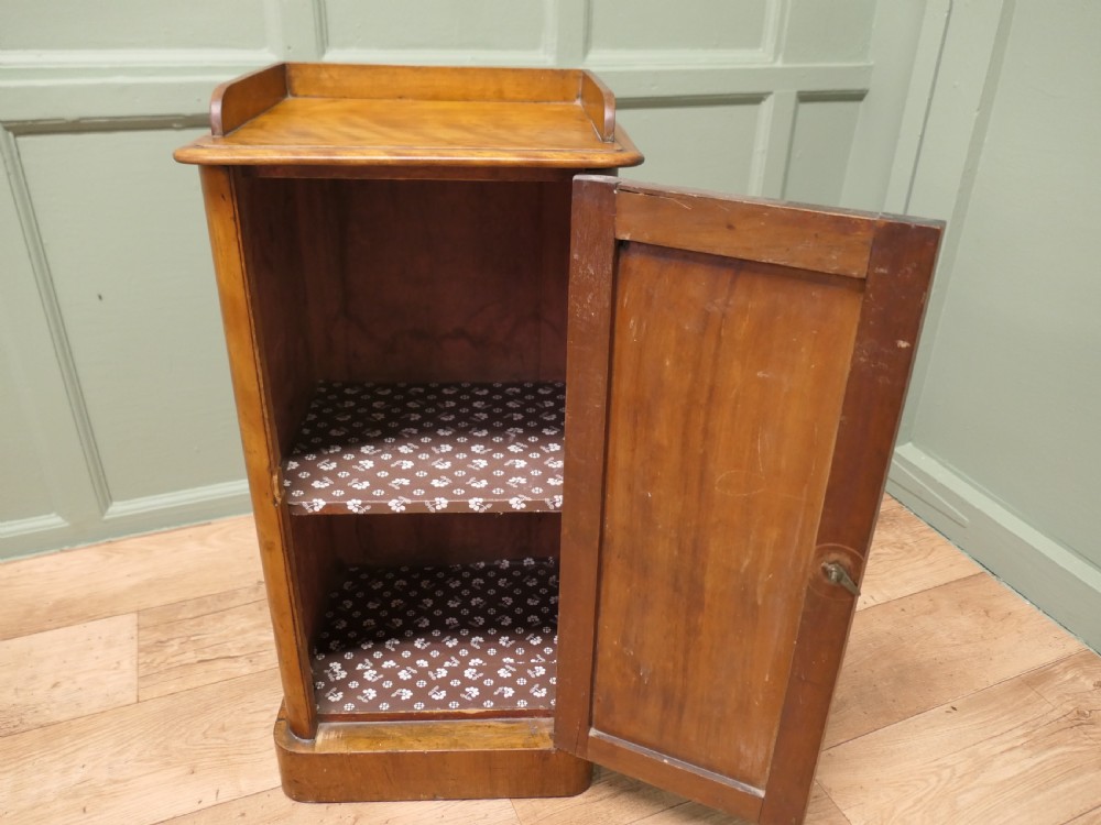 A Victorian birch bedside cupboard featuring a three-sided gallery top, a single panelled door with a glass handle, and a solid plinth base. View VI