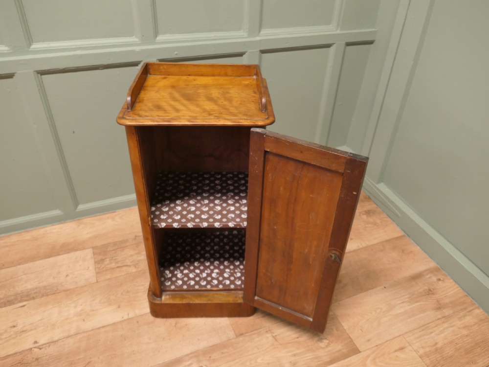 A Victorian birch bedside cupboard featuring a three-sided gallery top, a single panelled door with a glass handle, and a solid plinth base. View VII