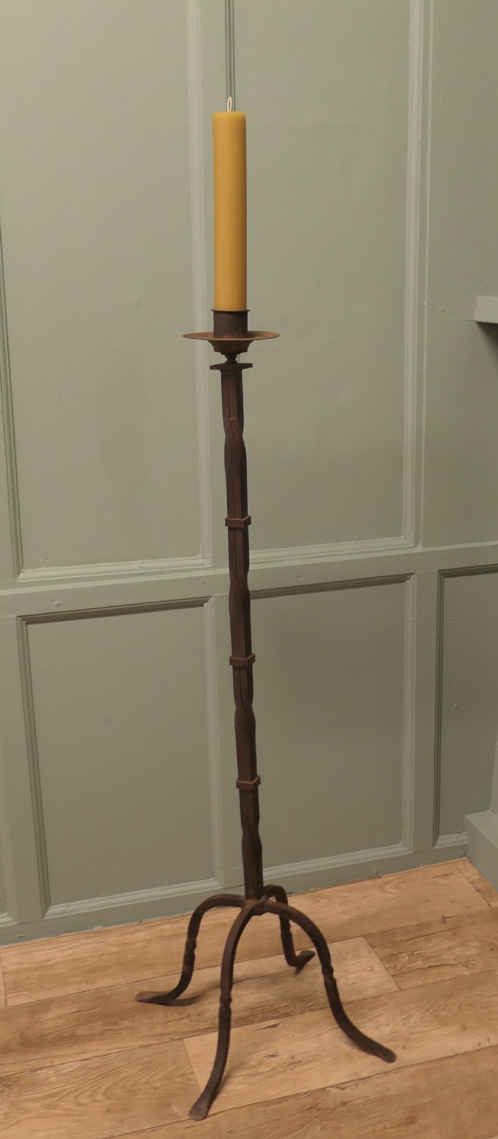 A tall hand-forged wrought iron floor candlestick with a twisted central stem, collar joins, a drip tray sconce, and a splayed tripod base.