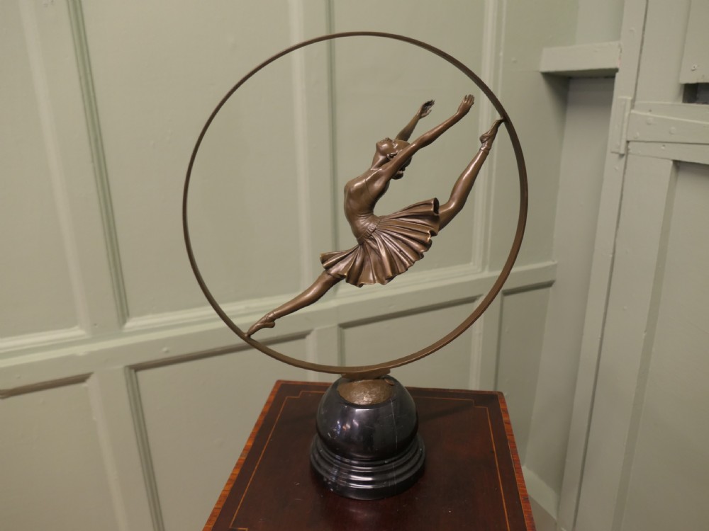 A bronze sculpture depicting a ballerina leaping inside a circular hoop, mounted on a turned black marble base.
