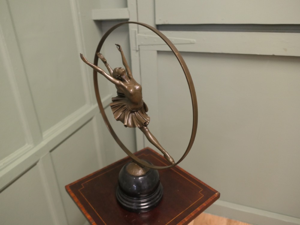 A bronze sculpture depicting a ballerina leaping inside a circular hoop, mounted on a turned black marble base. View III