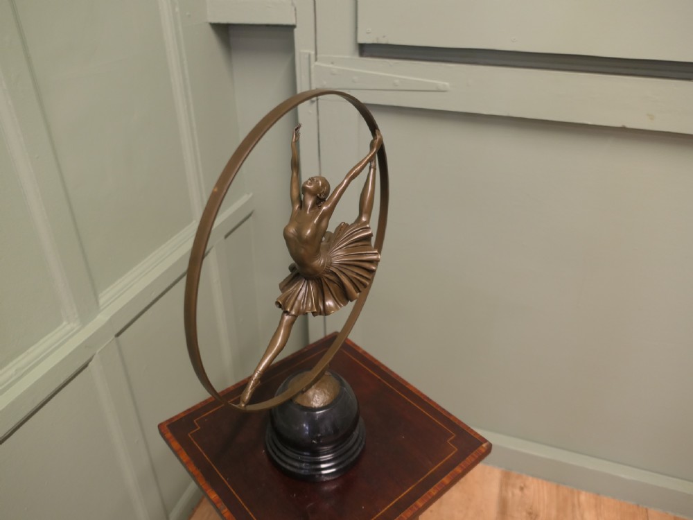 A bronze sculpture depicting a ballerina leaping inside a circular hoop, mounted on a turned black marble base. View IV