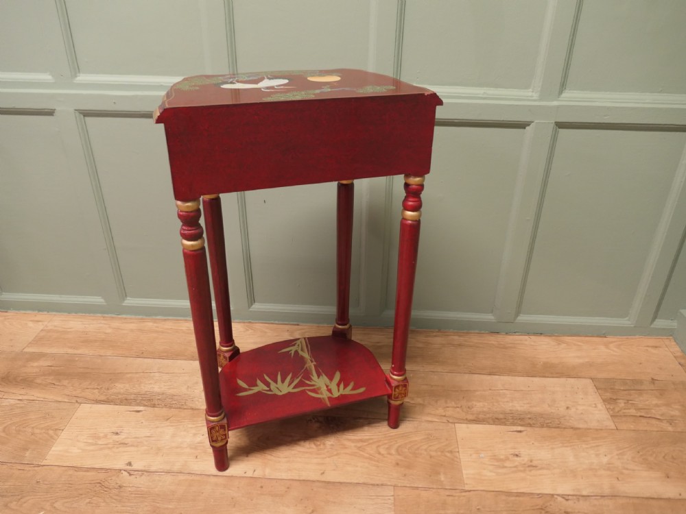 A tall red lacquer Chinoiserie side table featuring hand-painted crane and floral motifs, gilded turned legs, a single drawer, and an undershelf. View II