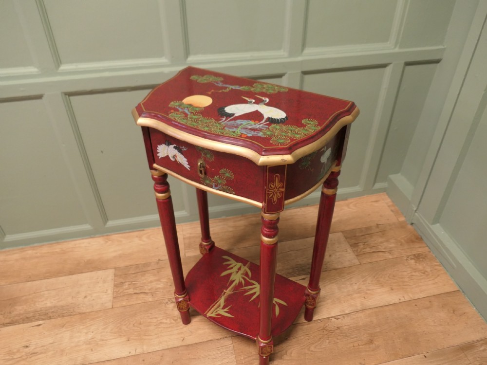 A tall red lacquer Chinoiserie side table featuring hand-painted crane and floral motifs, gilded turned legs, a single drawer, and an undershelf. View IV