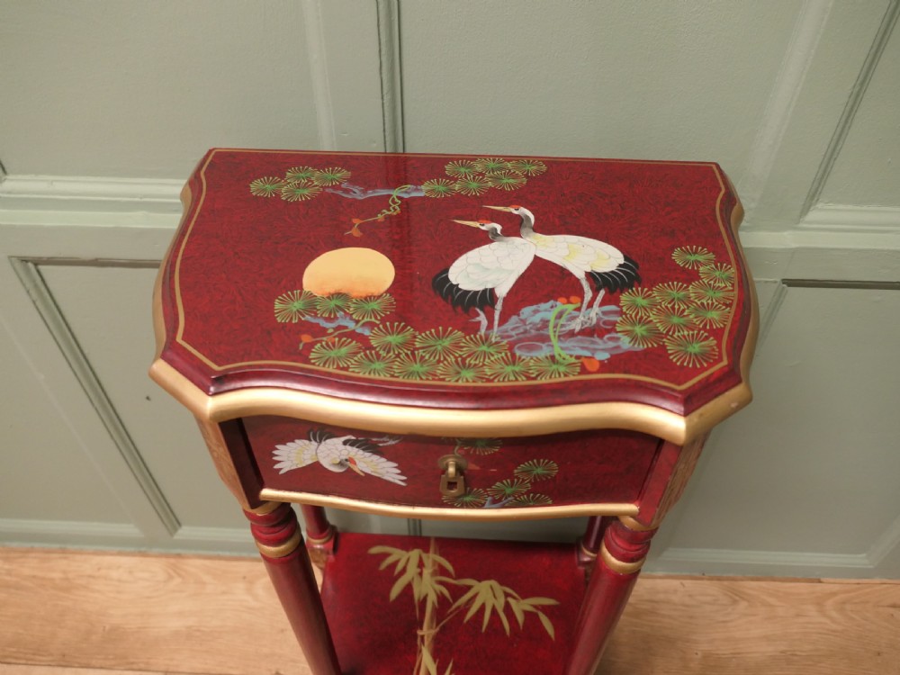 A tall red lacquer Chinoiserie side table featuring hand-painted crane and floral motifs, gilded turned legs, a single drawer, and an undershelf. View VI