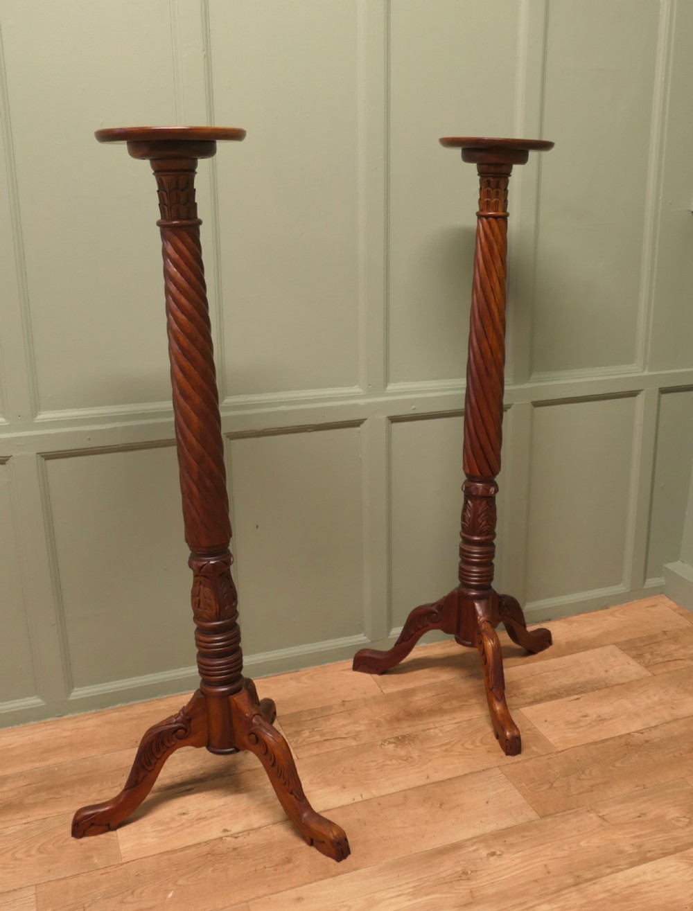 A pair of tall carved mahogany torchere stands featuring spiral shafts, foliate carving, and tripod cabriole bases.