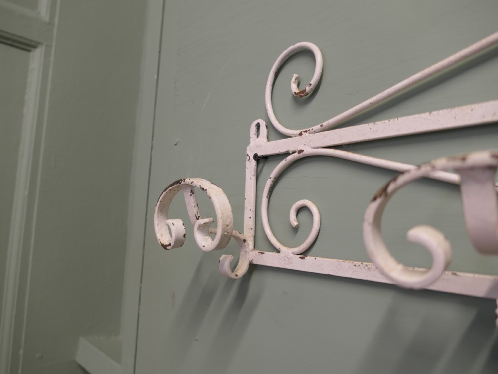 A long, wall-mounted off-white wrought iron hat and coat rack featuring scrollwork detailing and multiple curved hooks. View V