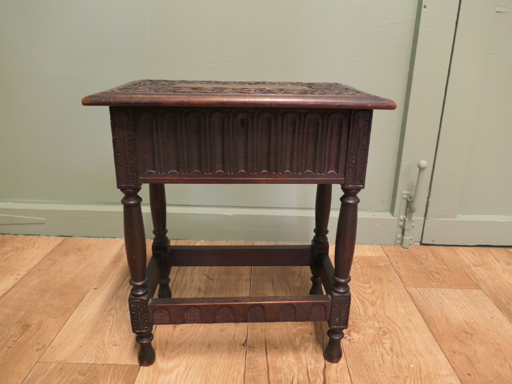 A dark carved oak joint stool featuring a carved rectangular top, a deep fluted apron with a keyhole, turned baluster legs, and lower stretchers.