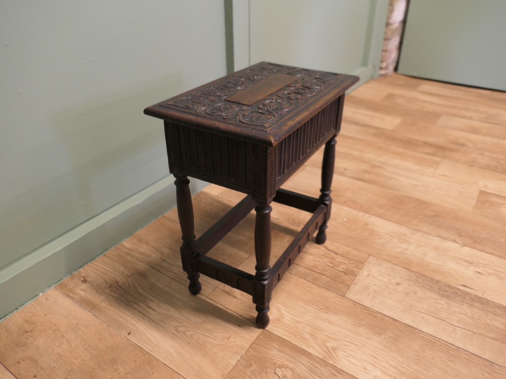 A dark carved oak joint stool featuring a carved rectangular top, a deep fluted apron with a keyhole, turned baluster legs, and lower stretchers. View II