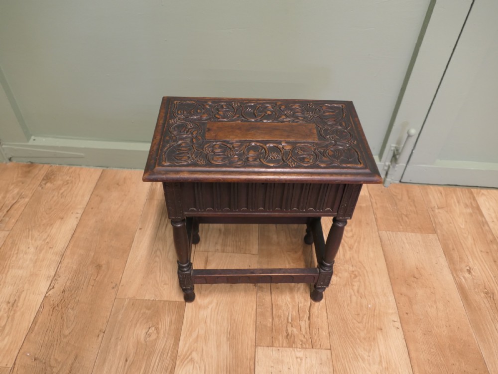 A dark carved oak joint stool featuring a carved rectangular top, a deep fluted apron with a keyhole, turned baluster legs, and lower stretchers. View III