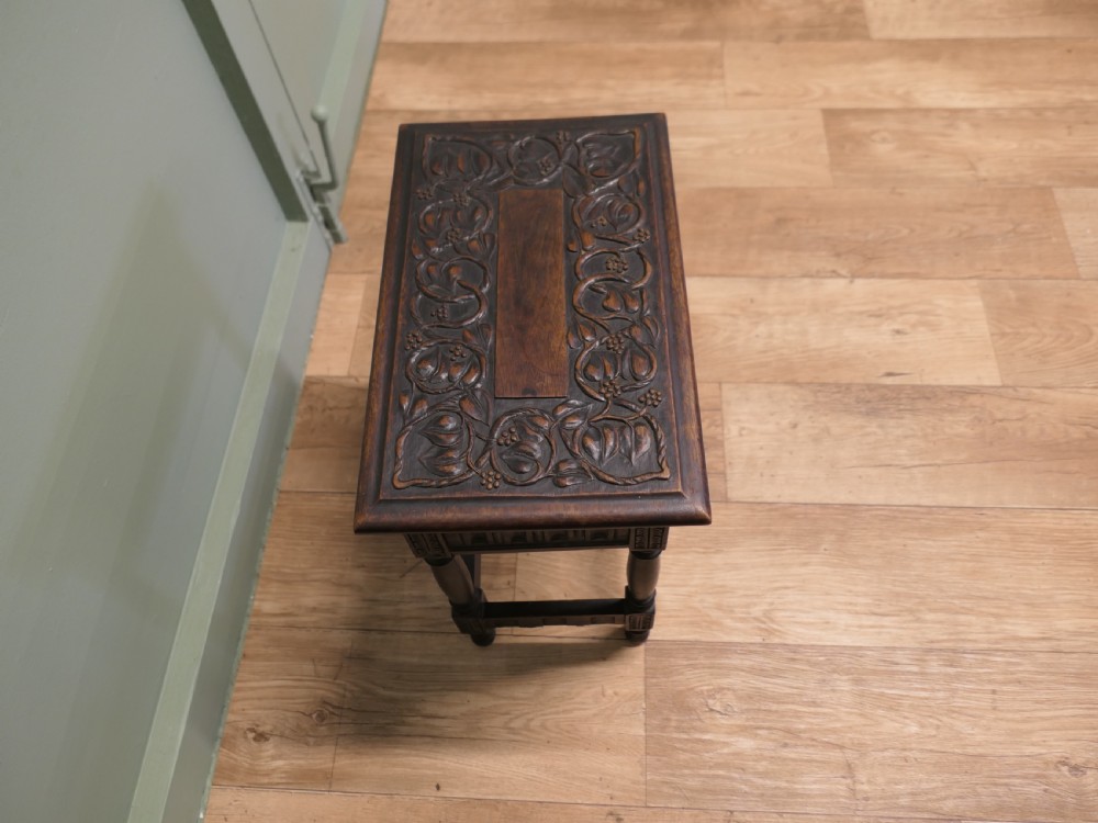 A dark carved oak joint stool featuring a carved rectangular top, a deep fluted apron with a keyhole, turned baluster legs, and lower stretchers. View IV