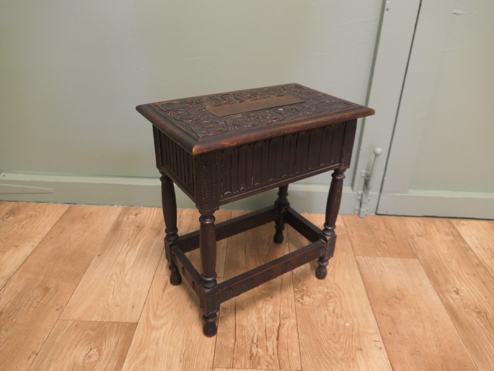 A dark carved oak joint stool featuring a carved rectangular top, a deep fluted apron with a keyhole, turned baluster legs, and lower stretchers. View V