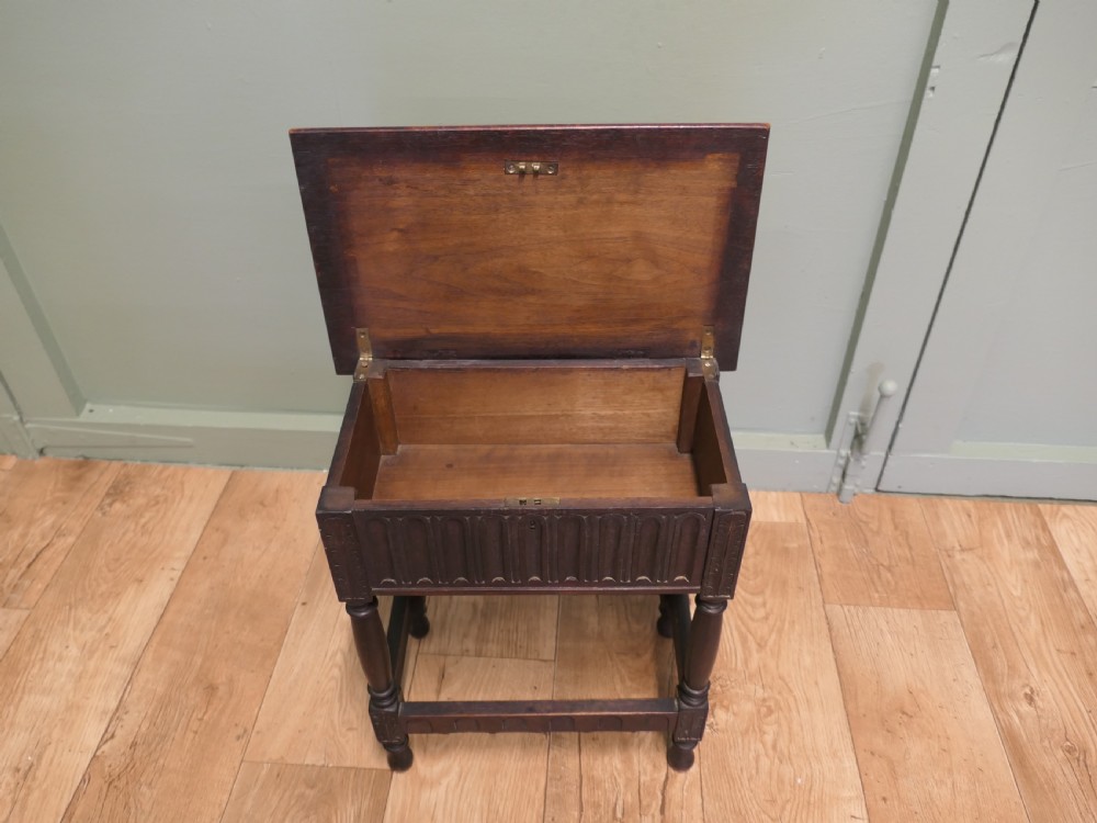 A dark carved oak joint stool featuring a carved rectangular top, a deep fluted apron with a keyhole, turned baluster legs, and lower stretchers. View VI