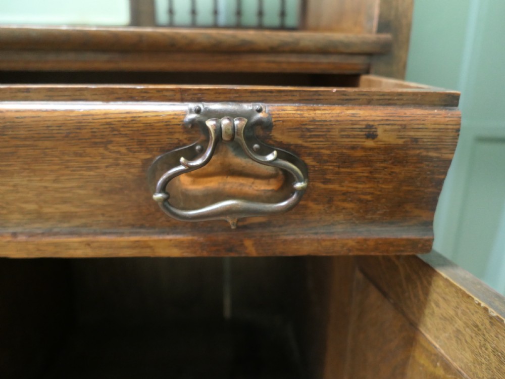 A large Arts and Crafts oak sideboard featuring a mirrored back, upper leaded glass cabinets, carved lower cupboard doors with botanical motifs, and brass handles. View IV