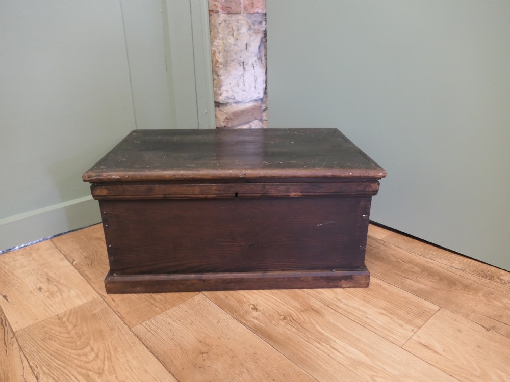 A rectangular dark stained pine carpenters box with a hinged lid and a moulded plinth base.