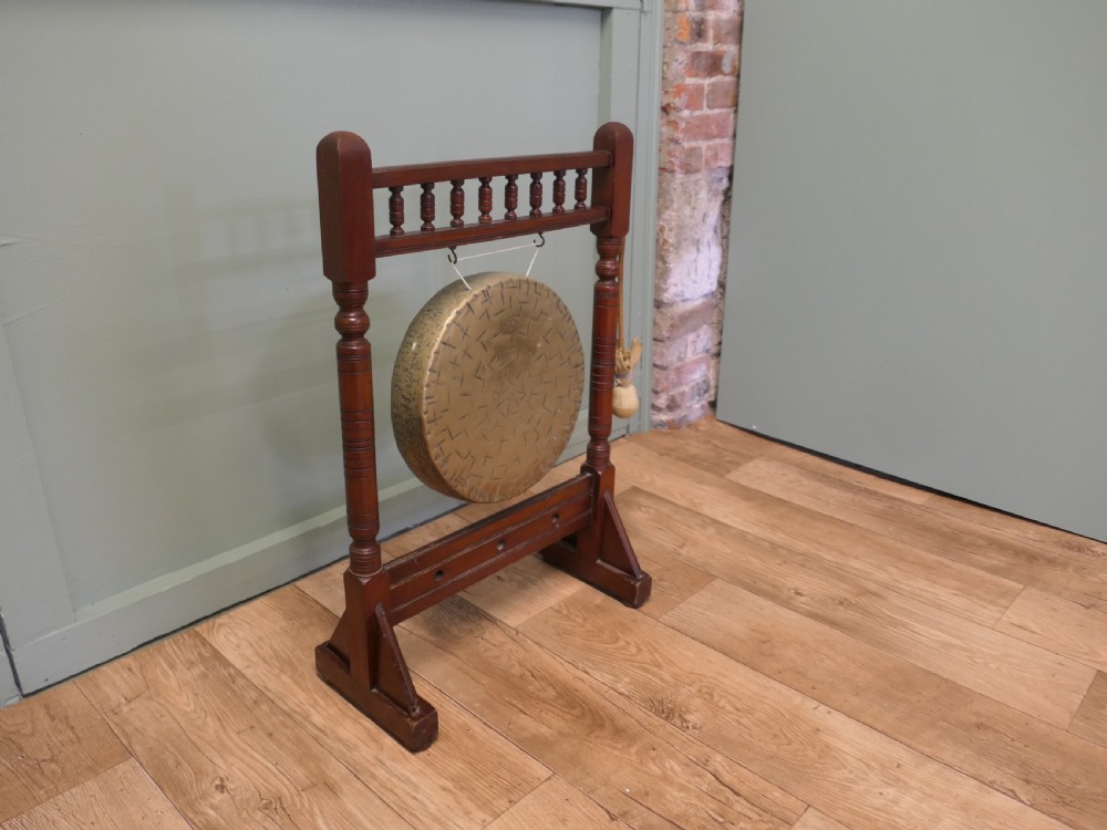 An Arts and Crafts dark timber floor frame featuring turned upper spindles and holding a central suspended hammered brass circular gong disc with an attached striker. View III