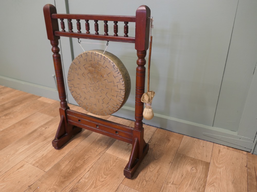 An Arts and Crafts dark timber floor frame featuring turned upper spindles and holding a central suspended hammered brass circular gong disc with an attached striker. View IV