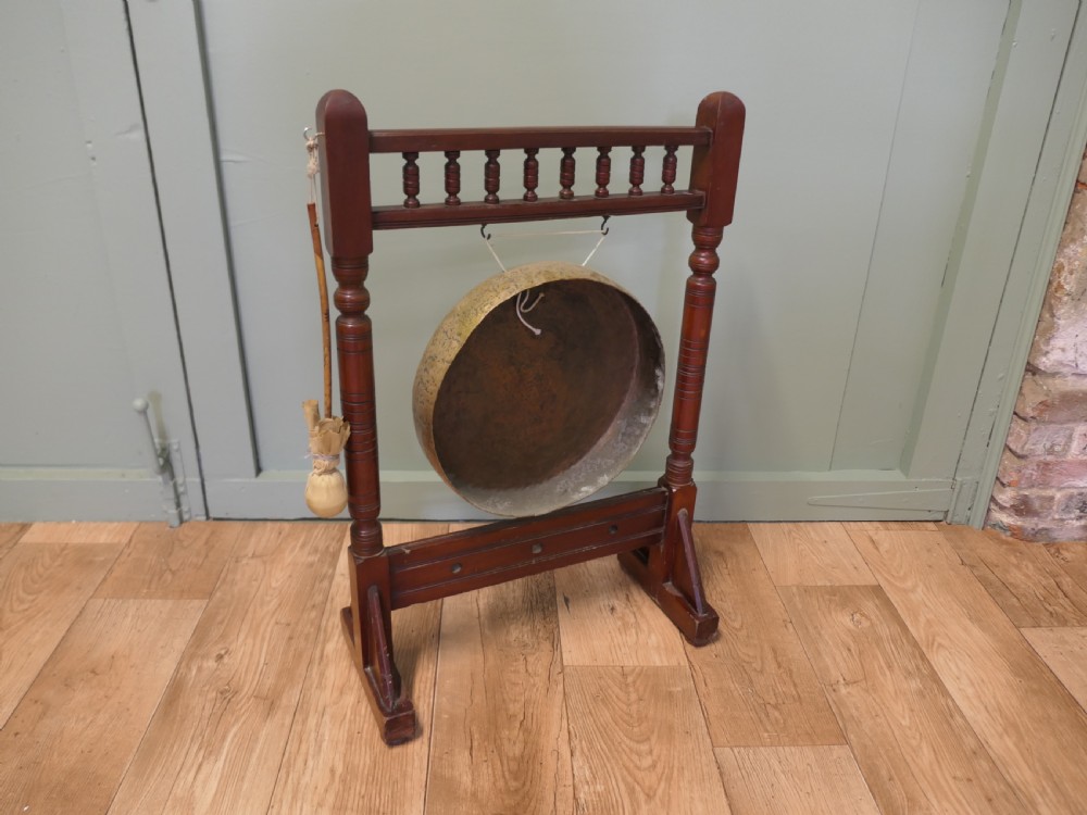 An Arts and Crafts dark timber floor frame featuring turned upper spindles and holding a central suspended hammered brass circular gong disc with an attached striker. View V