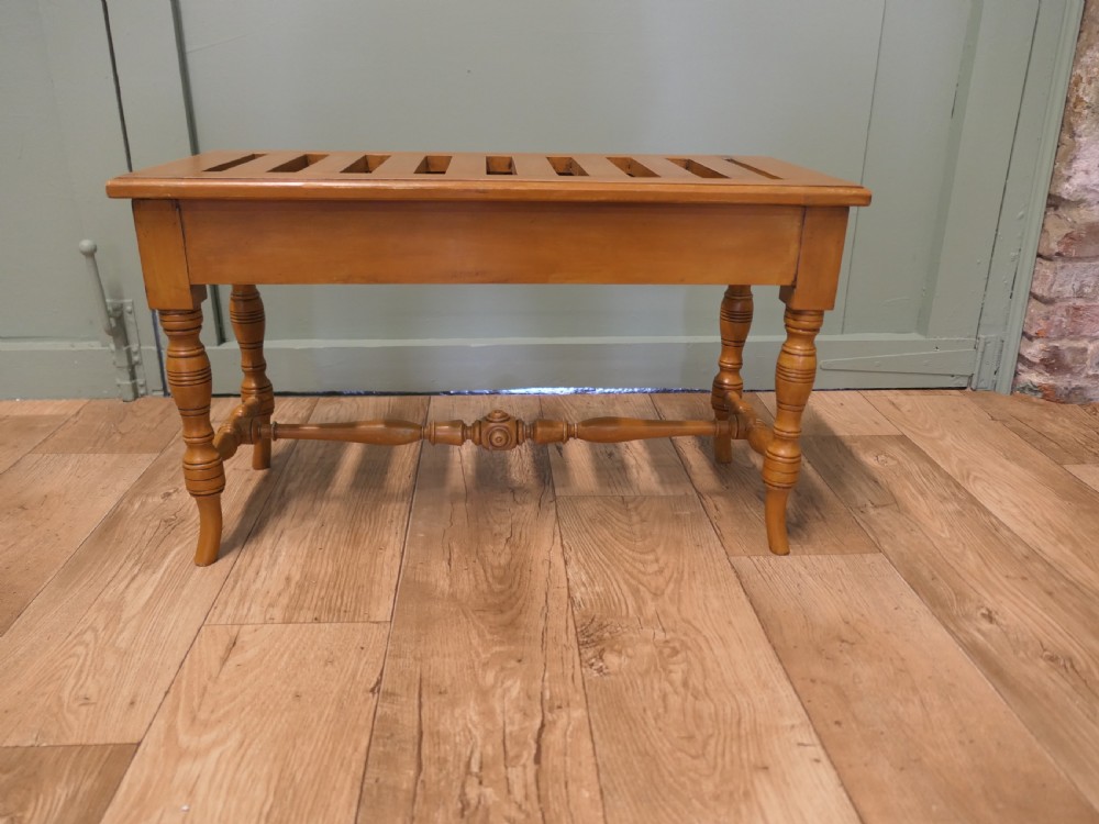 A golden oak Arts and Crafts luggage rack featuring a slatted top surface, turned legs, and a turned central stretcher.