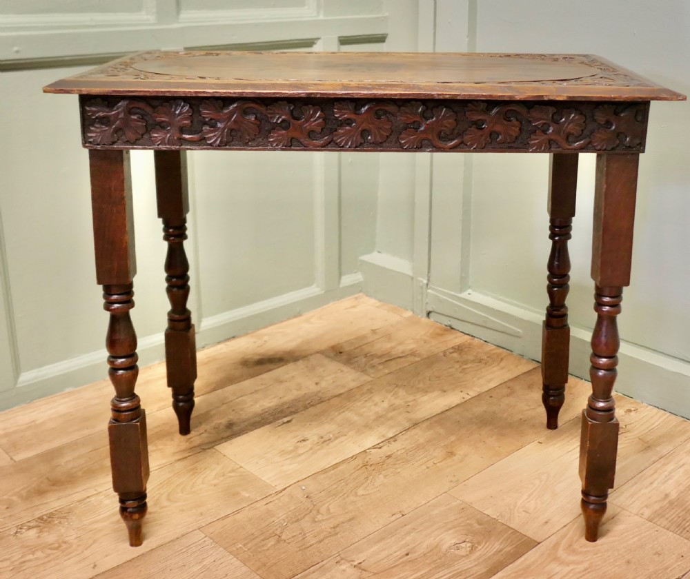 A rectangular dark elm side table featuring intricately carved Celtic scrollwork along the apron and tabletop border, supported by turned legs. View VI
