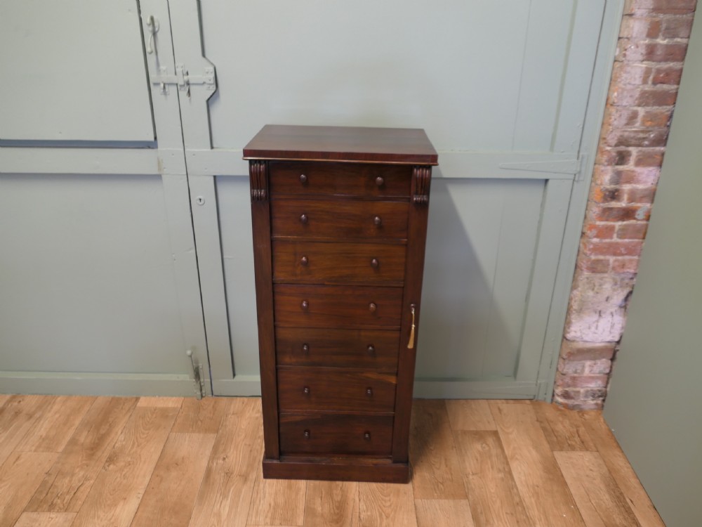 A tall Victorian mahogany Wellington chest featuring seven graduated drawers, turned wooden knob handles, and a side locking bar with a key.