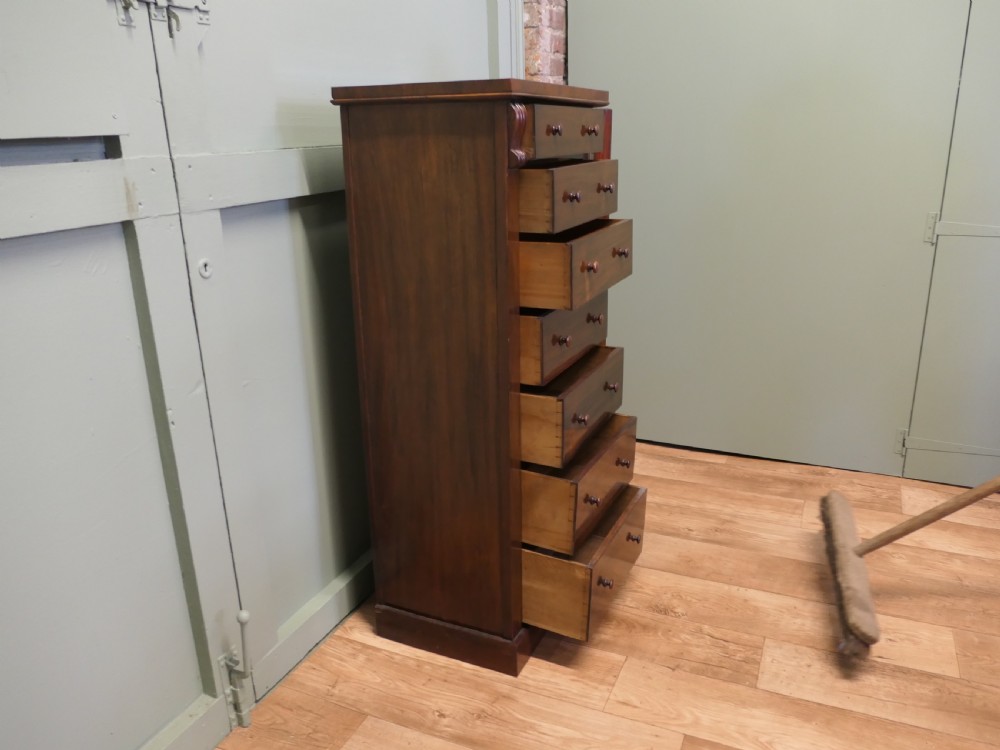 A tall Victorian mahogany Wellington chest featuring seven graduated drawers, turned wooden knob handles, and a side locking bar with a key. View IV